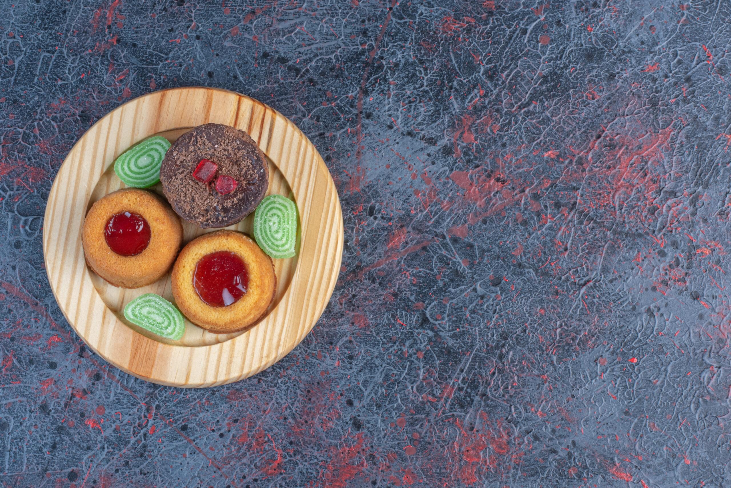 Various cakes and marmalades on a wooden platter on abstract background